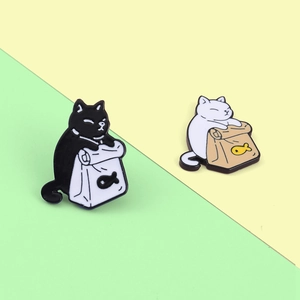 Close-up of cute enamel cat pins featuring black and white kittens with fish bags