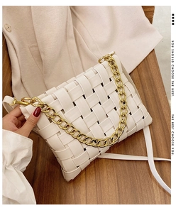 Detail of white woven leather handbag with chunky gold chain strap on wooden surface