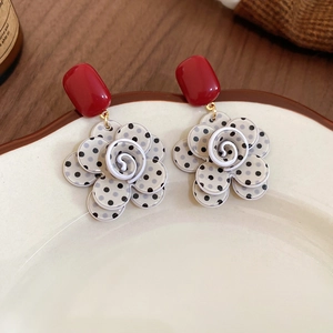 Detailed close-up of retro floral tassel earrings with red studs on a ceramic plate