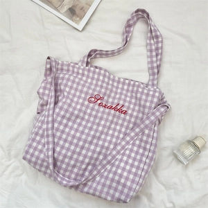 Detail of purple plaid tote bag showing red embroidered logo and versatile dual straps