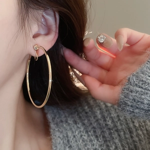 Close-up of a large gold hoop clip-on earring worn on an ear showing metallic shine