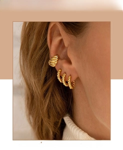 Detail showing a trio of layered golden twisted C-shape hoop earrings on a model's ear