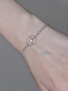 Detailansicht eines Armbands mit hohler Metallblume und Perle am Handgelenk getragen