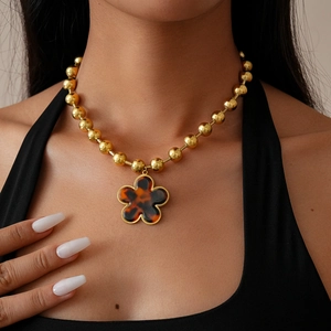 Close-up of a vintage clover flower pendant on a golden bead chain necklace worn by a model