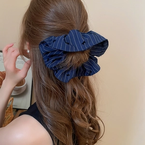 Vue détaillée d'un chouchou bleu à rayures avec broderie de nœud sur cheveux bouclés