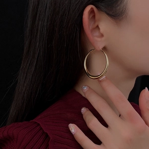 Close-up of a model wearing large polished gold hoop earrings in a minimalist metal style