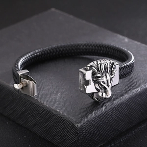 Détail de l'emblème tête de lion argentée sur bracelet en cuir tressé noir pour homme