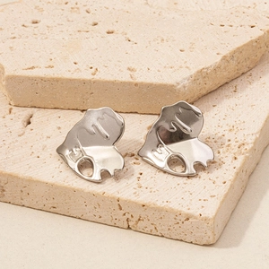 Detailed close-up of irregular silver heart earrings on beige natural stone blocks