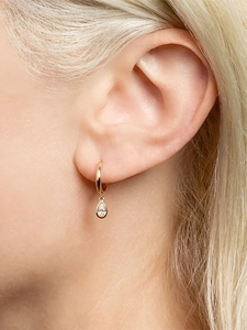 Close-up of gold pear-cut drop earrings with sparkling zircon stones on a model