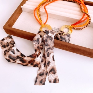 Detail of beaded necklace with leopard print ribbon and gold rings on a velvet tray