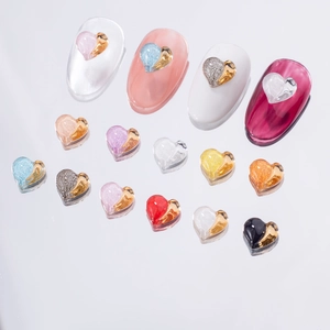Colorful heart-shaped resin nail charms with gold borders and sample manicure display
