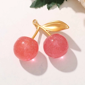 Macro shot of pink glitter cherry charms with golden leaves on a textured surface