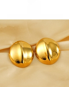 Macro shot of gold-plated stainless steel oval stud earrings on luxury champagne silk fabric