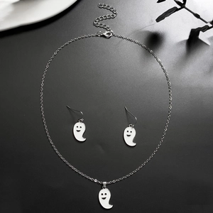 Close-up of white enamel ghost necklace and earrings set on a black textured surface