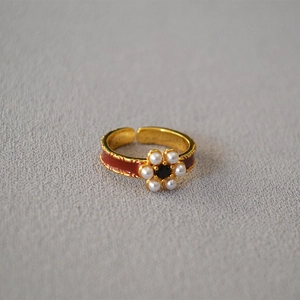 Detail of vintage gold-plated ring with red enamel inlay and pearl flower center