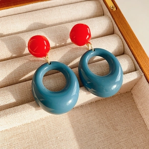 Detail of red stud and teal resin oval hoop earrings in a wooden jewelry box