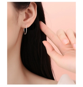 Close-up of minimalist S999 sterling silver hoop earring worn on a soft pink background