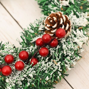 Close-up of frosted pine wreath with red berries and snowy pinecone for holiday decor
