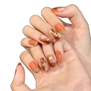 Short oval press-on nails with orange marble design, gold foil, and metallic accents