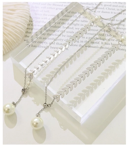 Detail of silver phoenix-tail wheat chain necklace with white pearls on a paper background