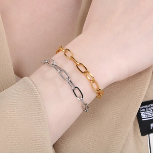 Close-up of gold and silver rectangular link chain bracelets on model wearing a beige blazer