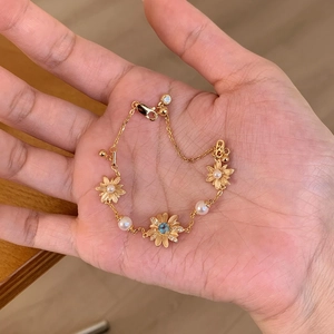 Detailed view of elegant gold daisy bracelet with pearls and a blue stone on hand