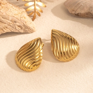 Elegant gold teardrop earrings with embossed wave pattern on minimalist rock texture