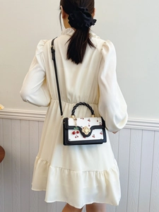 Sweet cherry print crossbody bag with floral clasp and braided handle on cream dress