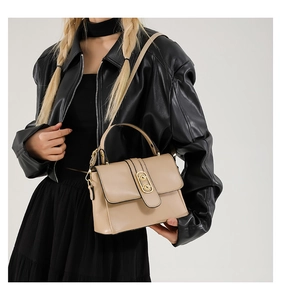 Close-up of beige crossbody bag with gold twist lock on model in black leather jacket