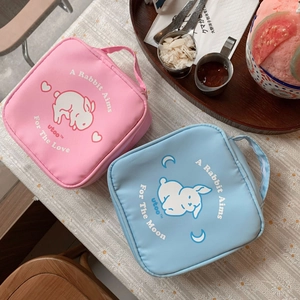 Detail of pink and blue rabbit cosmetic bags with handles on a floral tablecloth