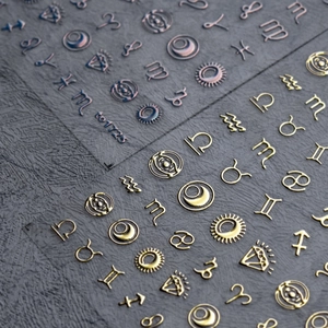 Dettaglio macro di adesivi nail art celesti dorati e iridescenti con segni zodiacali