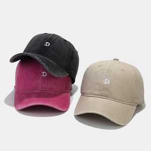 Close-up of stacked baseball caps in black, pink, and khaki with white D letter embroidery