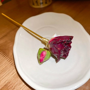 Dettaglio di un fermaglio per capelli vintage con rosa rosso scuro e perla su piatto bianco