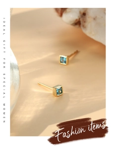 Macro detail of geometric gold earrings featuring square blue zircon stones