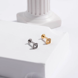 Detailed view of G23 titanium square stud earrings with central crystal on a marble pedestal