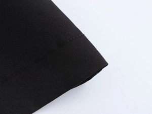 Detailed macro view showing the clean double-stitched hem and woven texture of the black dress
