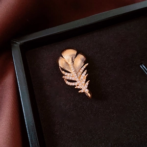Macro shot of 18k gold plated feather brooch with white zircons on black velvet