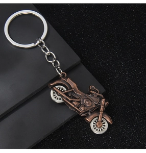 Close-up of a bronze metal motorcycle keychain on a matte black background with sparkles