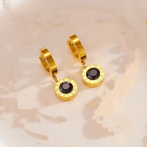Detailed close-up of golden roman numeral earrings with black faceted gemstones