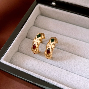 Macro detail of gold-plated quilted C-shape earrings with red and green gemstones