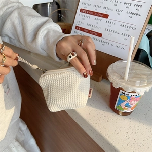 Détail d'un porte-monnaie blanc gaufré avec fermeture éclair et cordon tenu à la main