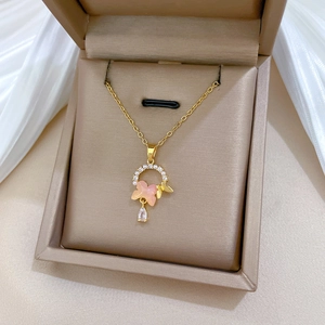 Detail of gold necklace featuring pink butterfly, pearls, and a teardrop crystal