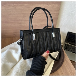 Detailed view of hand holding a black quilted leather handbag with silver hardware accents