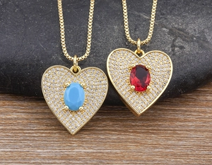 Close-up of gold heart pendants with turquoise and ruby stones on a stone background