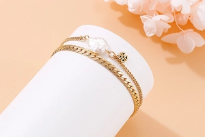 Detail of gold double-layered bracelet with baroque pearl and black clover charm