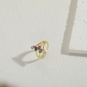 Detalle de anillo abierto dorado con cinco gemas ovales de colores sobre piedra blanca