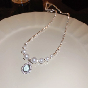 Detail of fan-shaped pearl necklace with a light blue zircon drop on a white plate