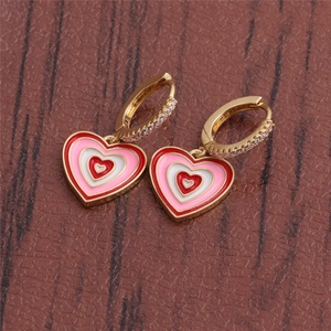 Detailed view of gold heart earrings with pink enamel and crystals on a wooden background