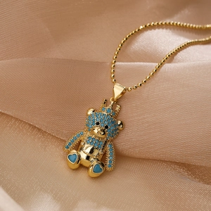 Collana dorata con pendente a forma di orso con corona e zirconi blu su sfondo champagne
