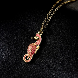 Golden seahorse pendant necklace with pink enamel details on a black leather texture